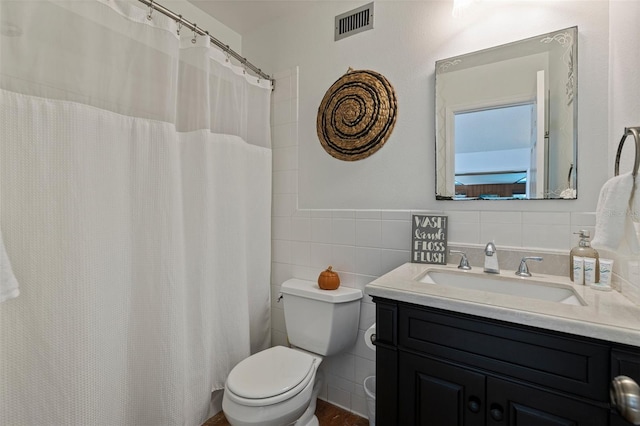 bathroom with visible vents, toilet, vanity, and tile walls