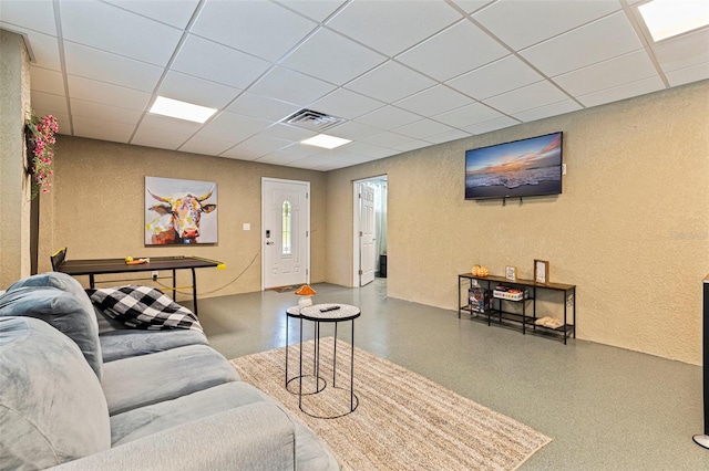 living area featuring a textured wall, a drop ceiling, and visible vents