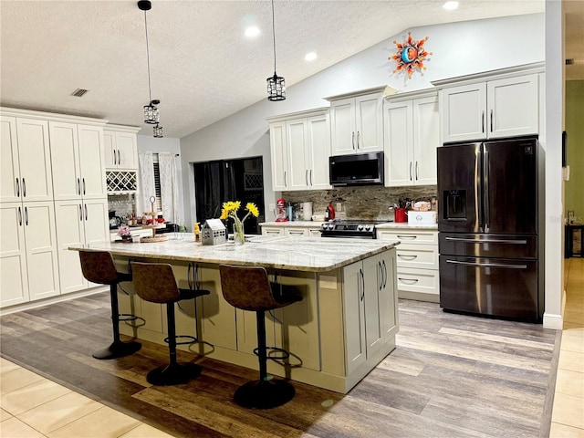 kitchen featuring an island with sink, vaulted ceiling, backsplash, and black fridge with ice dispenser