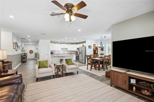 living room with light wood-type flooring, ceiling fan with notable chandelier, visible vents, and recessed lighting