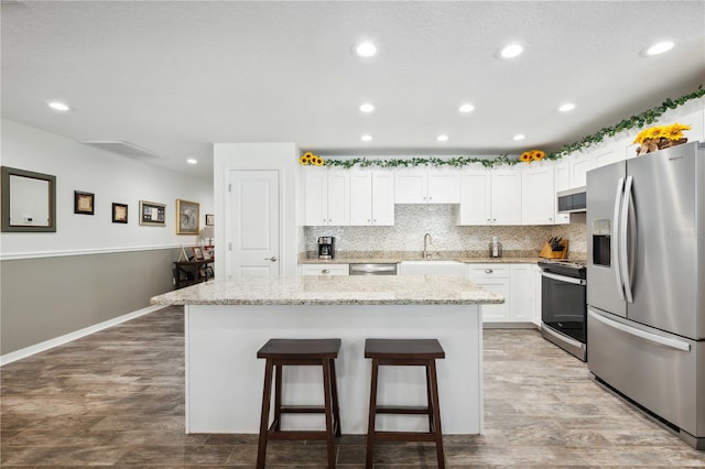 kitchen featuring tasteful backsplash, white cabinets, a center island, appliances with stainless steel finishes, and a sink