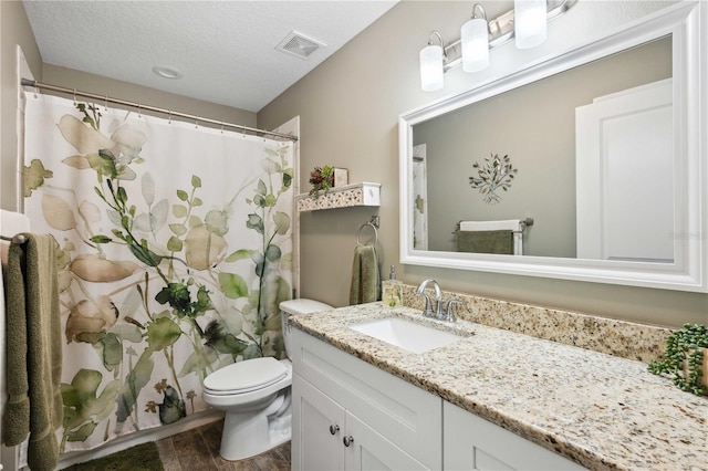 bathroom featuring visible vents, toilet, a textured ceiling, vanity, and wood finished floors