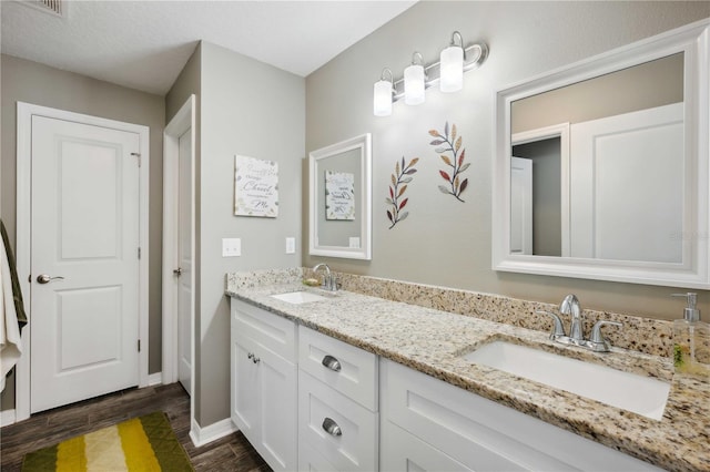 full bathroom with wood finished floors, double vanity, a sink, and baseboards