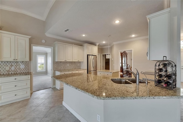 kitchen featuring freestanding refrigerator, ornamental molding, visible vents, light stone counters, and a sink