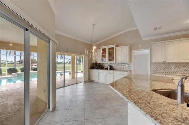 kitchen featuring visible vents, light stone counters, a sink, lofted ceiling, and decorative backsplash