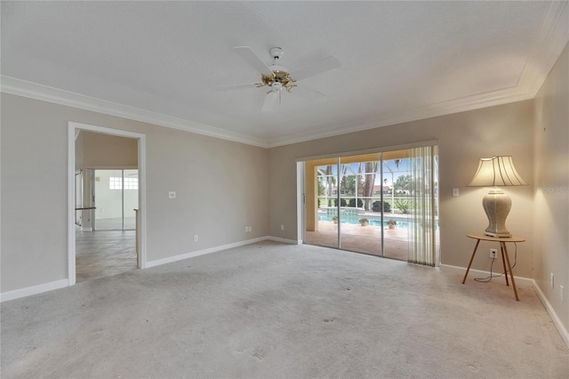 carpeted spare room with baseboards, ornamental molding, and a ceiling fan