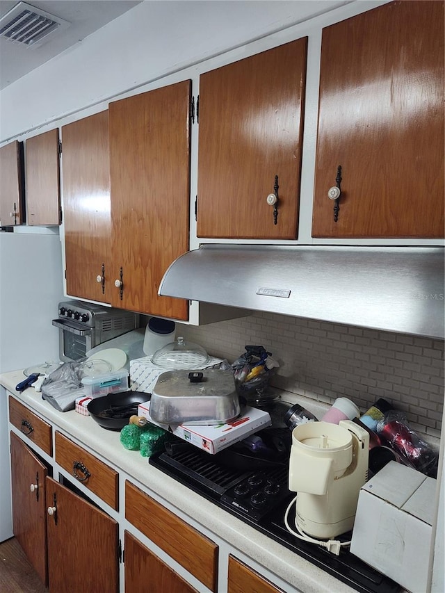 kitchen with brown cabinets, visible vents, light countertops, and decorative backsplash