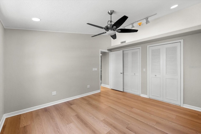 unfurnished bedroom with two closets, light wood-type flooring, baseboards, rail lighting, and recessed lighting