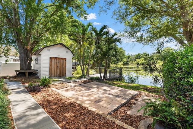 view of patio featuring a shed, a water view, fence, and an outbuilding