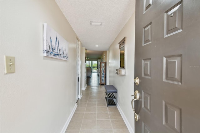 hallway with a textured ceiling, light tile patterned floors, and baseboards