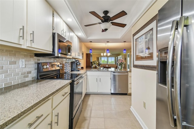 kitchen with appliances with stainless steel finishes, light tile patterned floors, a tray ceiling, ceiling fan, and a sink