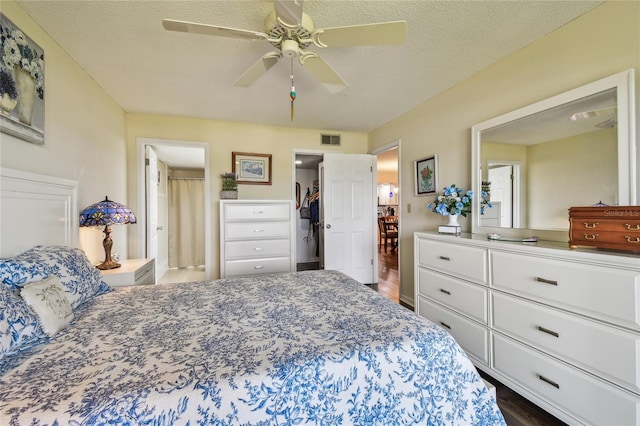 bedroom featuring dark wood-style floors, visible vents, a textured ceiling, and ceiling fan