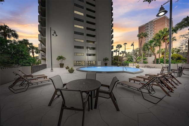 pool at dusk featuring a community pool and a patio