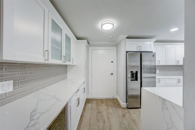 kitchen featuring glass insert cabinets, white cabinets, stainless steel fridge, and light stone countertops