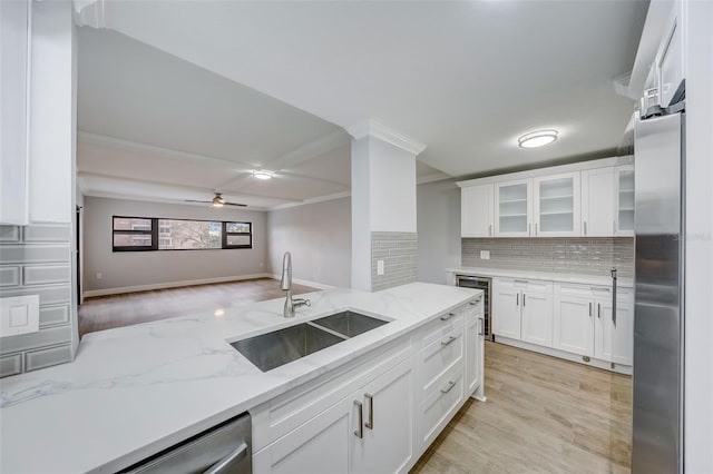 kitchen with tasteful backsplash, white cabinets, wine cooler, appliances with stainless steel finishes, and a sink