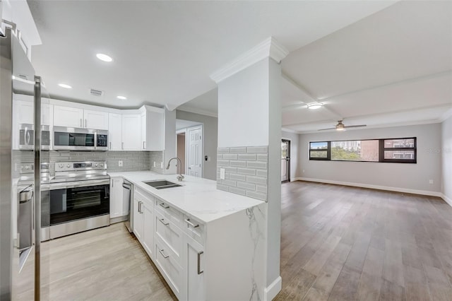kitchen featuring appliances with stainless steel finishes, a sink, open floor plan, light wood finished floors, and backsplash