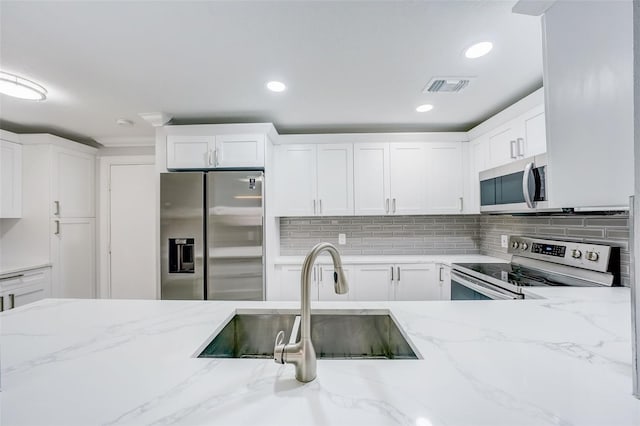 kitchen with white cabinets, visible vents, a sink, stainless steel appliances, and decorative backsplash