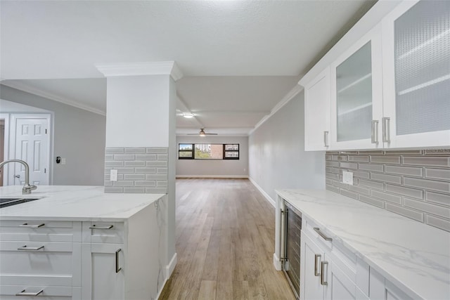 kitchen with light stone counters, glass insert cabinets, crown molding, white cabinets, and light wood finished floors