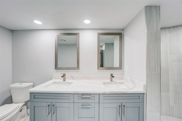 bathroom featuring a sink, toilet, double vanity, and a tile shower