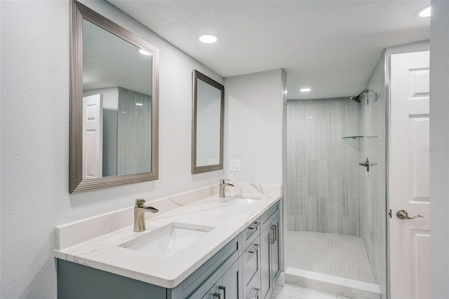bathroom with recessed lighting, double vanity, a tile shower, and a sink