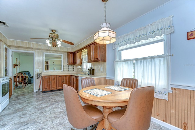 dining room with visible vents, a ceiling fan, wooden walls, crown molding, and wainscoting