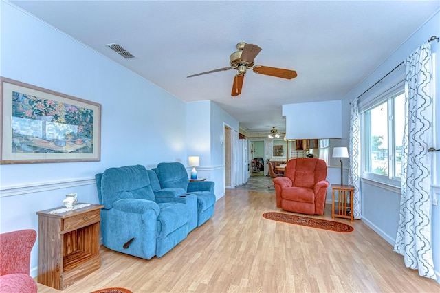 living room featuring light wood-style floors, visible vents, baseboards, and ceiling fan