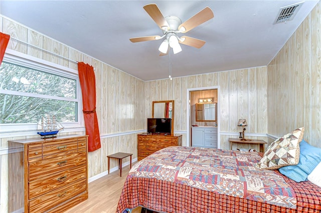 bedroom featuring wood finished floors, wooden walls, ensuite bathroom, and visible vents