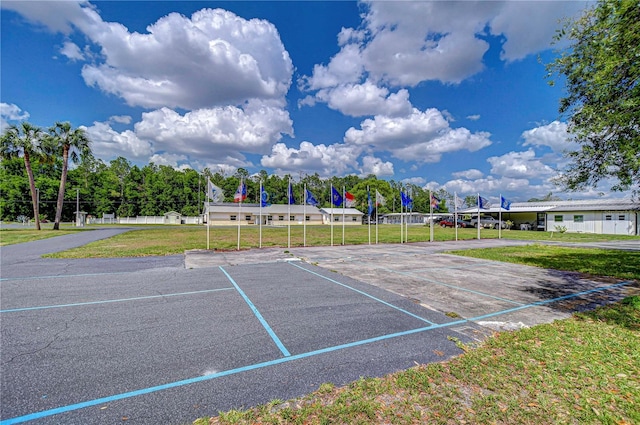 view of community with fence, uncovered parking, and a lawn