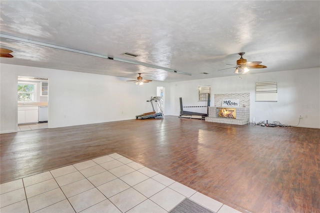 unfurnished living room with a brick fireplace, visible vents, wood finished floors, and ceiling fan