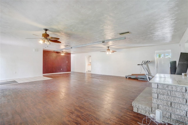 unfurnished living room featuring visible vents, a ceiling fan, wood finished floors, and a textured ceiling