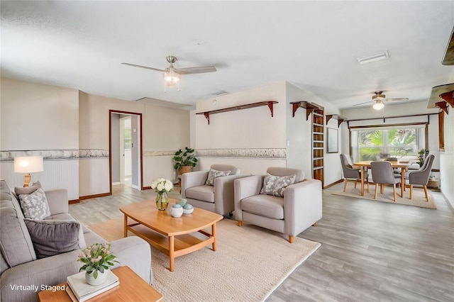 living area featuring baseboards, light wood-style flooring, visible vents, and a ceiling fan
