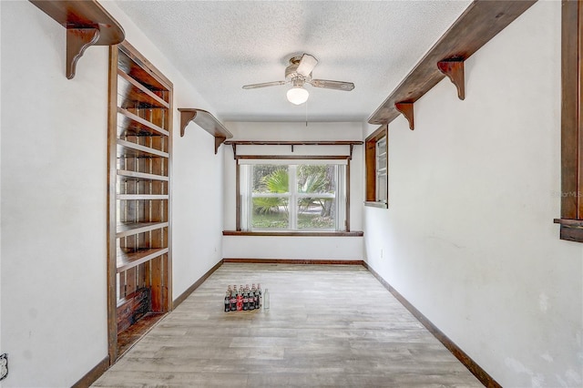 interior space featuring baseboards, a ceiling fan, wood finished floors, and a textured ceiling