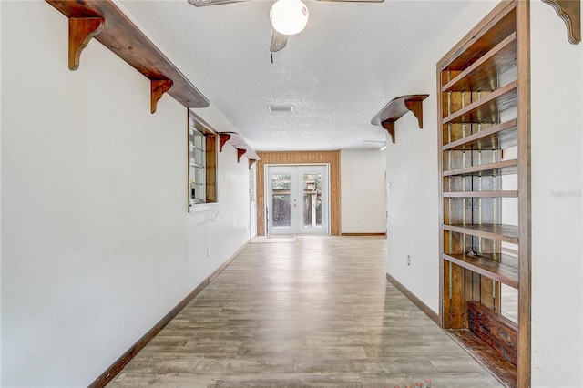 hall featuring baseboards, french doors, a textured ceiling, visible vents, and wood finished floors