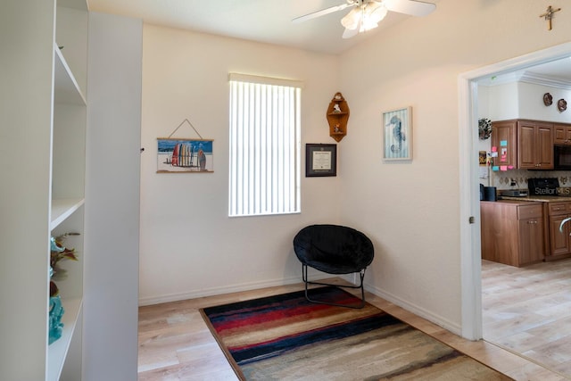 living area featuring light wood finished floors, a ceiling fan, and baseboards
