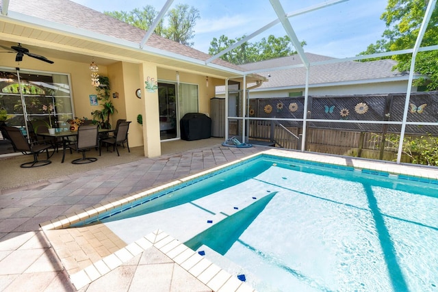 view of swimming pool featuring glass enclosure, a patio, fence, and ceiling fan
