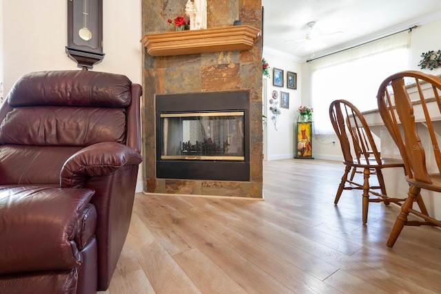 sitting room featuring crown molding, wood finished floors, a ceiling fan, a glass covered fireplace, and baseboards