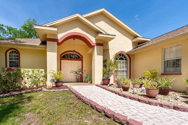 entrance to property featuring stucco siding and roof with shingles