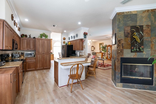 kitchen featuring black appliances, a peninsula, ornamental molding, a kitchen bar, and light wood finished floors