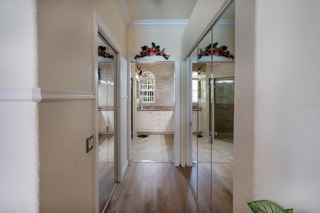 corridor with ornamental molding, light wood-style flooring, and a textured wall