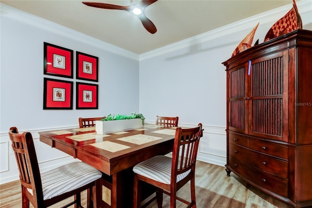 dining area with light wood-type flooring, a ceiling fan, wainscoting, and ornamental molding