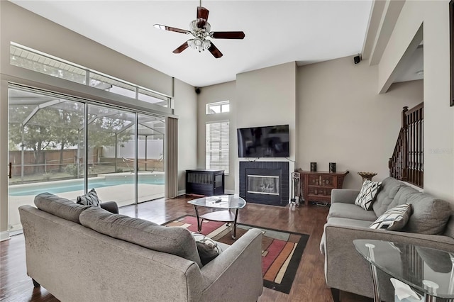 living area with wood finished floors, ceiling fan, a tiled fireplace, and baseboards