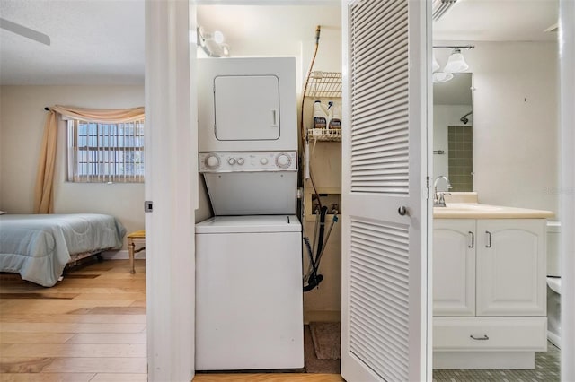 clothes washing area featuring laundry area, a sink, light wood finished floors, and stacked washer / dryer
