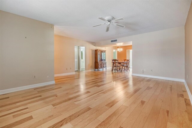 unfurnished living room featuring a ceiling fan, a textured ceiling, visible vents, baseboards, and light wood-style floors