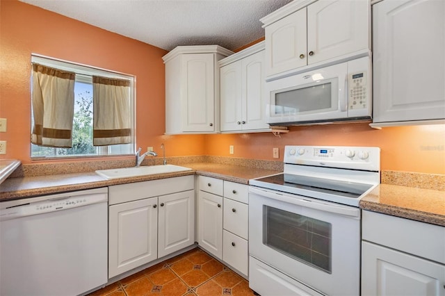 kitchen with tile patterned flooring, white appliances, a textured ceiling, white cabinets, and a sink