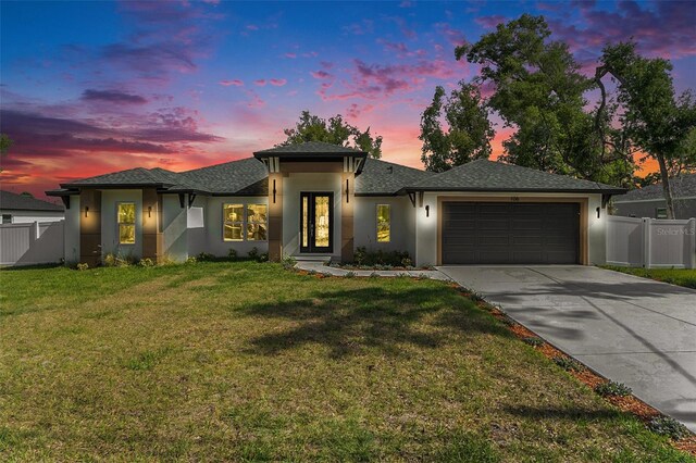 prairie-style house featuring driveway, a lawn, a garage, fence, and stucco siding