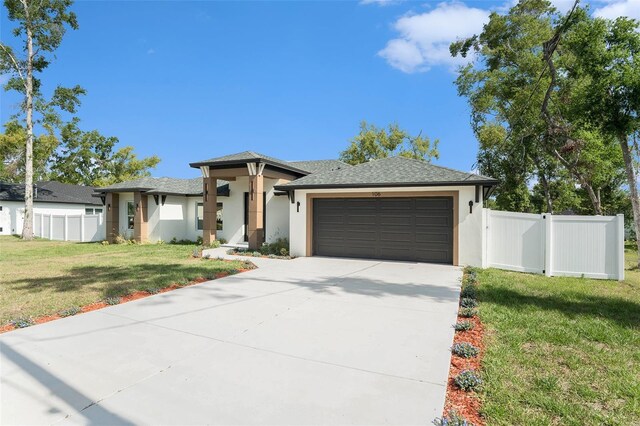 prairie-style house with a garage, a front lawn, fence, stucco siding, and driveway