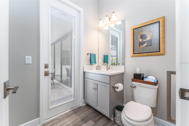 bathroom featuring baseboards, wood finished floors, toilet, and vanity