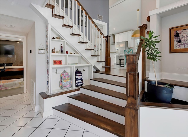 stairs with tile patterned flooring, a towering ceiling, baseboards, and visible vents