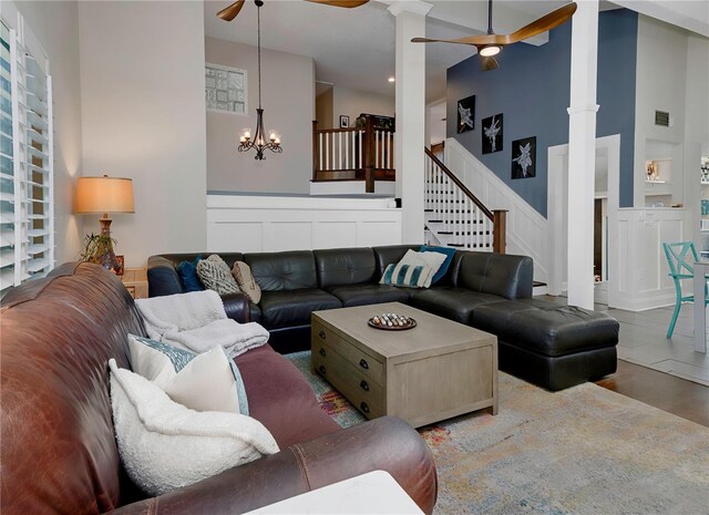 living room featuring visible vents, a decorative wall, ceiling fan with notable chandelier, and a high ceiling