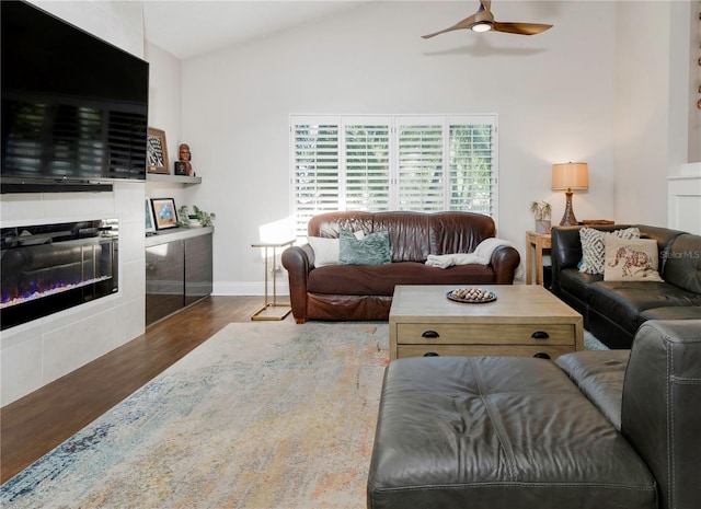 living area with lofted ceiling, wood finished floors, a ceiling fan, baseboards, and a tile fireplace